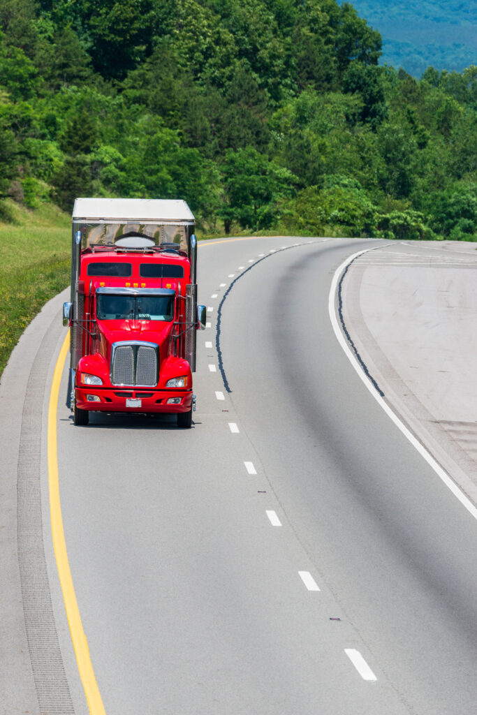 A lone red 18-wheeler travels a Tennessee interstate. Note: All logos and identifying marks removed from the vehicle. Image is designed to provide a generous amount of copy space all around the truck.